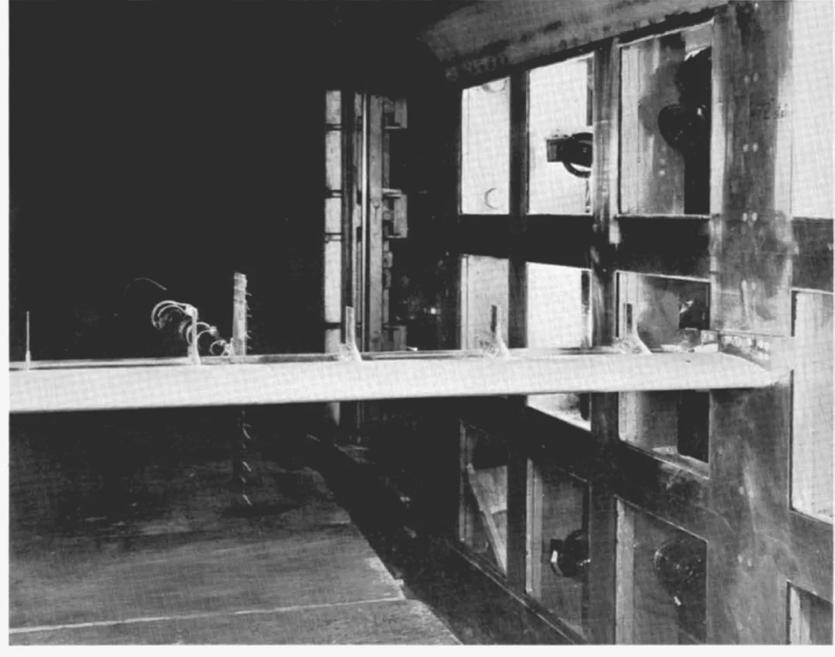 Photograph of a full-span airfoil model mounted across the test section of a large wind tunnel, with struts and wall windows